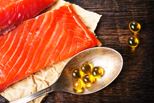 Salmon fillet and fish oil capsules on a metal spoon, representing natural sources for fish oil production.