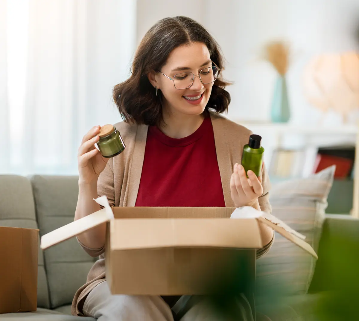 Woman sitting on a sofa opening a parcel and checking beauty products from a shipped order.