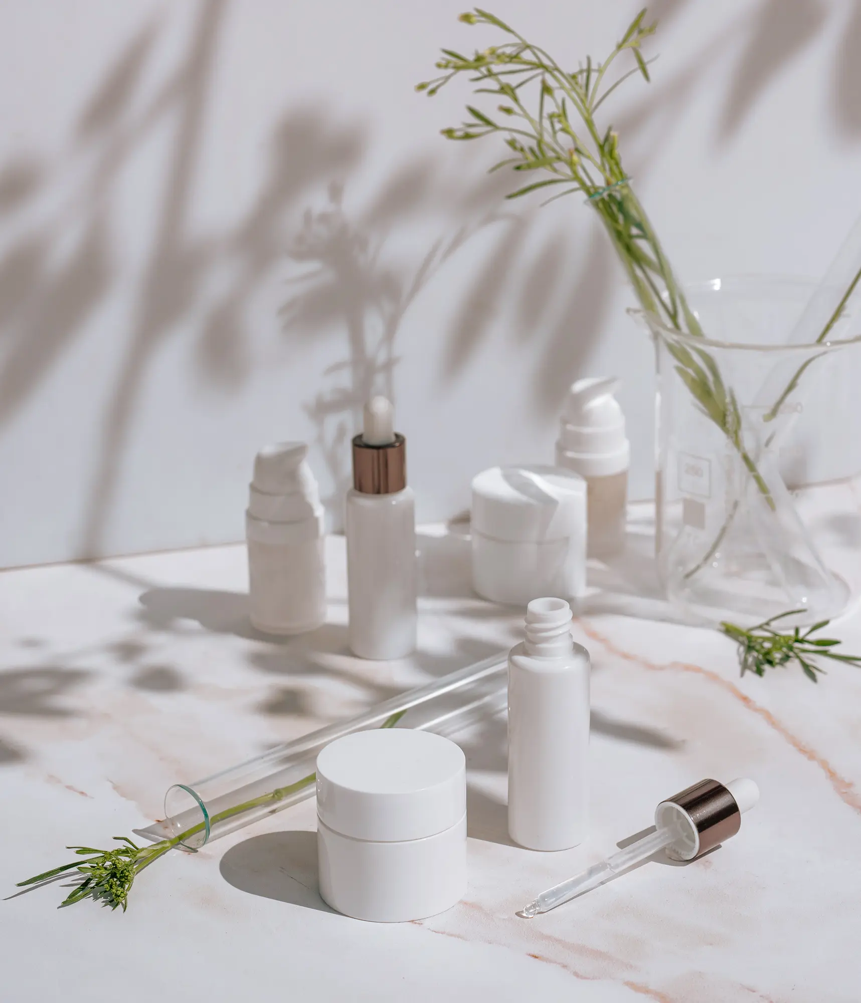 Skincare line prototypes in white packaging with laboratory glassware and natural ingredients during product development