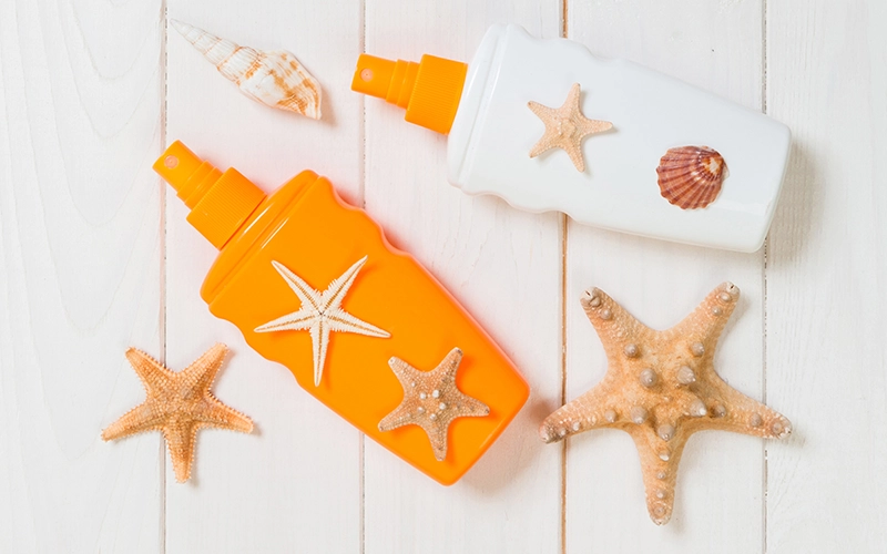 Sunscreen spray bottles with seashells and starfish on a light wooden surface