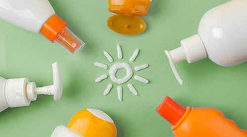 Various sunscreen bottles and dispensers arranged around a sun symbol on a green background
