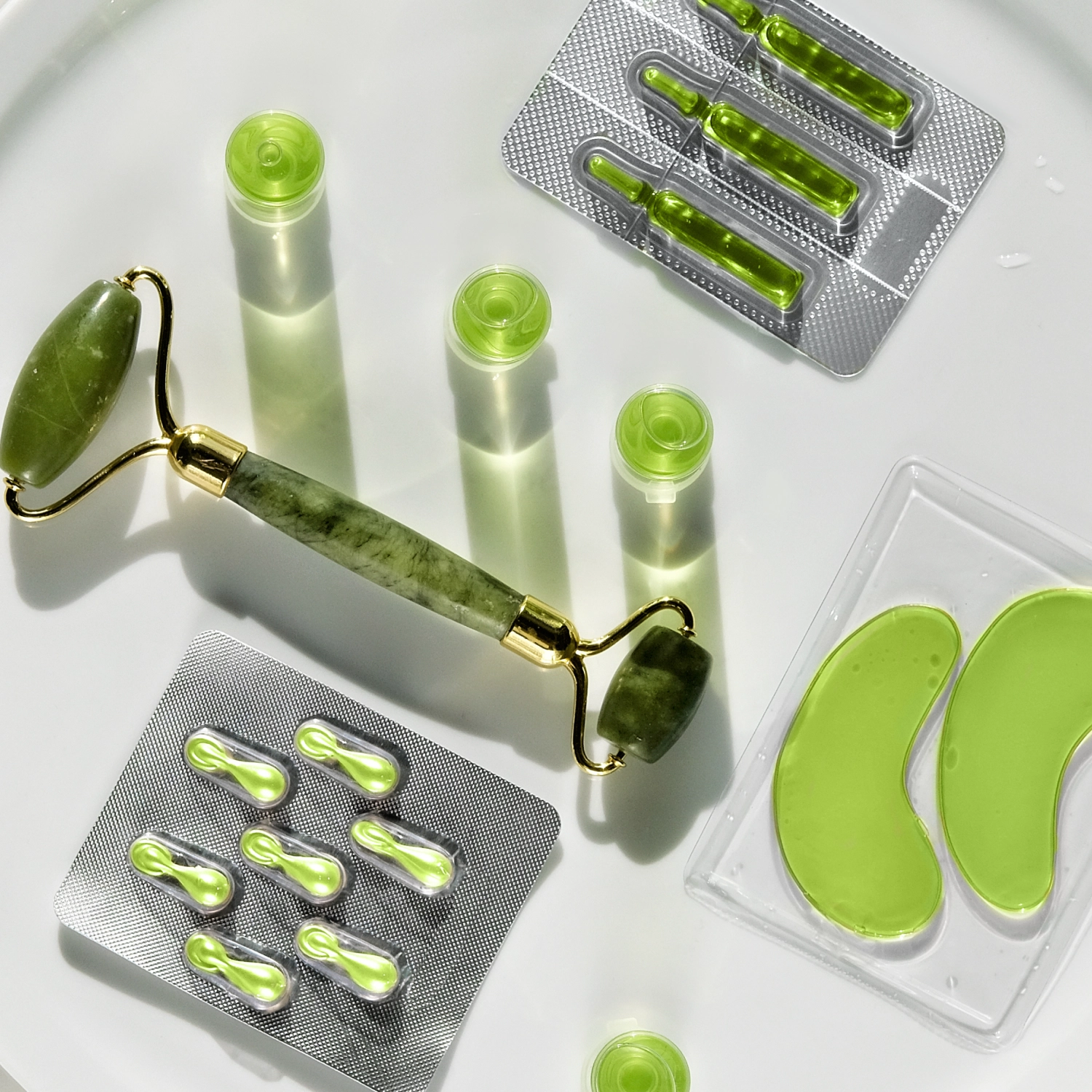 Green skincare products flatlay — jade roller, ampoules, serum vials and eye patches
