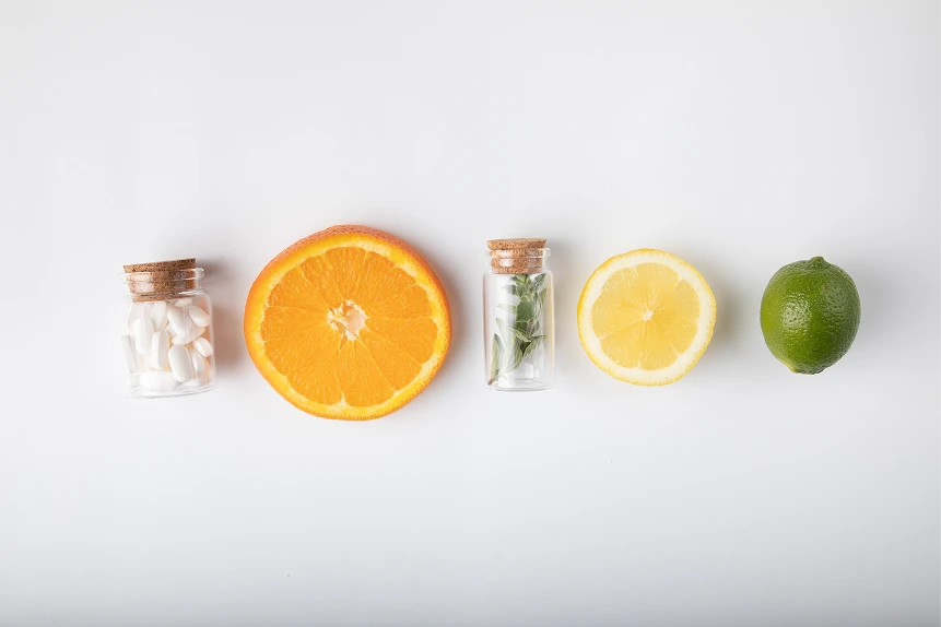Small glass jars, an orange slice, a lemon slice, and a lime arranged on a white background.