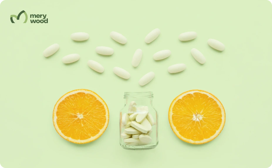 White vitamin tablets in a small glass jar with orange halves on a light green background.
